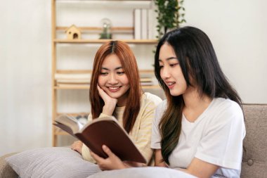 Genç lezbiyen çift evde oturma odasındaki büyük rahat kanepede oturup dinlenirken birlikte kitap okuyorlar..
