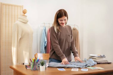 Kadın tasarımcı, ev atölyesinde yeni bir koleksiyon tasarlarken gömlek boyutunu ölçmek ve ayrıntıları kontrol etmek için mezura kullanıyor.