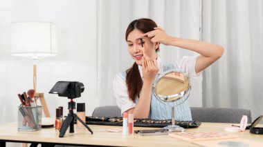 Genç güzellik etkileyicisi, sosyal medyada ya da web blogcusu stüdyoda paylaşmak üzere kameraya video kaydederken kaş fırçası kullanarak kozmetik ürünü test edip tavsiye ediyor..