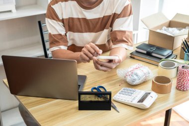 Erkek girişimci akıllı telefonu kontrol etmek ve çevrimiçi siparişler almak için kullanıyor. Ürünü paketlemek ve paketlemek için alışveriş merkezinde çevrimiçi alışveriş yaparken müşteri göndermek için hazırlanıyor..