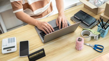 Erkek girişimci, kontrol etmek ve çevrimiçi siparişleri almak için dizüstü bilgisayar kullanıyor. Ürünü paketlemek için ev ofisinde çevrimiçi alışveriş yaparken müşteri göndermeye hazırlanıyor..