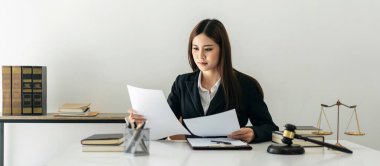 İş kadını avukat, avukatlık bürosunda pirinç pulları ve adalet çekiciyle masaya otururken iş sözleşmesini okumakla yükümlü..