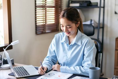 İş kadını, yeni iş projeleri hakkında bilgi okuyup belgelere not alırken, aynı zamanda iş muhasebe ve modern ofiste dizüstü bilgisayarlar üzerinde düşünceli bir şekilde çalışıyor..