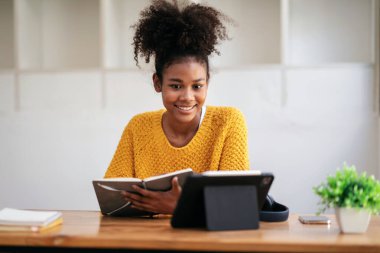 Kazaklı Afro-Amerikalı bir kadın üniversitede bilgi ve eğitimi öğrenirken online tablet dersine çalışmayı ve not defterine not almayı öğreniyor..