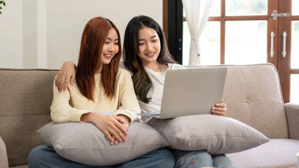 stock image Young woman lesbian couple sitting to embracing and watching movie or entertainment on laptop while spending time to relaxation together on big comfortable sofa at home.