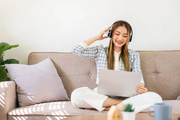 stock image Woman wearing headphones to relaxing with listening the music and watching entertainment on laptop while sitting on the comfortable sofa to leisure with cozy lifestyle in living room at home.