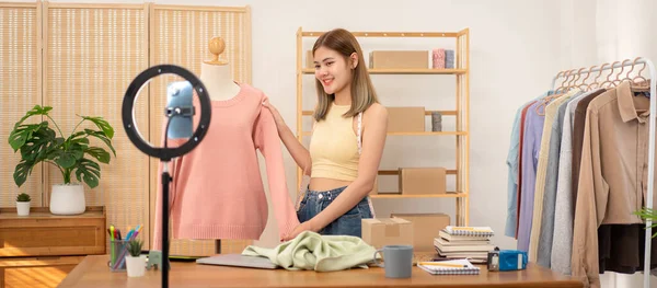 Woman designer entrepreneur showing sweater of new collection in mannequin and review product with detail while selling clothes product on live online social media streaming.