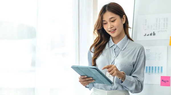 Confident businesswoman in suit reading business data on tablet to thinking and analysis about strategy and planning of new business while standing to working in modern office.
