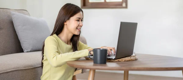 若い女性は床で笑顔に座っており 自宅のリビングルームでリラックスするためにオンラインで仕事や買い物をしながら ビジネスレポートを入力するためにラップトップを使用しています — ストック写真