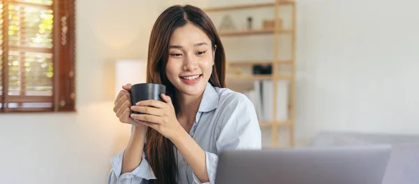 女性自由职业人士一边在家里的客厅里工作 一边在笔记本电脑上阅读商业数据 一边一边一边一边一边一边边喝着咖啡 — 图库照片