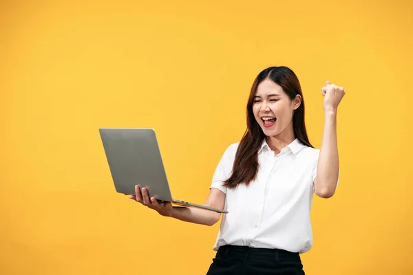 年轻的亚洲女人穿着白色短袖衬衫 拿着笔记本电脑一边工作 一边笑着 一边举起一只胳膊庆祝在黄色背景下独立工作的成功 — 图库照片