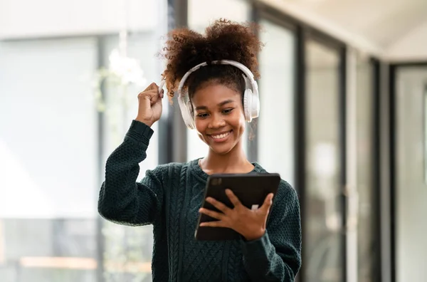 非洲裔美国女学生穿着毛衣和耳机 在大学学习教育和知识的同时 在线学习课程 并在数字平板电脑上写信息 — 图库照片