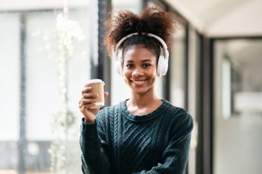 Afrika kökenli Amerikalı bir kadın, üniversitede eğitim ve bilgi dersi aldıktan sonra müzik dinlemek ve kahve içmek için süveter ve kulaklık takıyor..