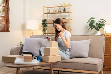 Genç girişimci akıllı telefonu online siparişleri kontrol etmek ve satış ürünlerinde başarılı bir şekilde kollarını kaldırırken aynı zamanda kanepede rahat bir şekilde oturuyor ve merkez ofisteki oturma odasında çalışıyor..