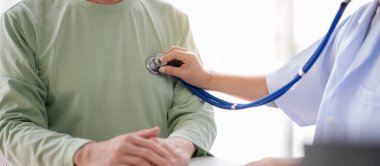 Yaşlı bir hastanın kalp atışlarını dinlemek için steteskop kullanan ve sağlık kontrolünden ve hastane panosuna reçete yazdıktan sonra yaşlılara sağlık hizmetlerini açıklayan kadın doktor..