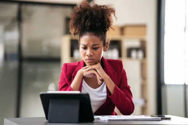 African american businesswoman in suit using digital tablet to reading accounting information of new business with stressful while working and thinking strategy of project in modern workspace.