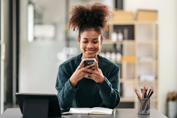 African american student woman in sweater using smartphone after watching e-learning and studying lesson online class on tablet while sitting to learning knowledge and education in university.