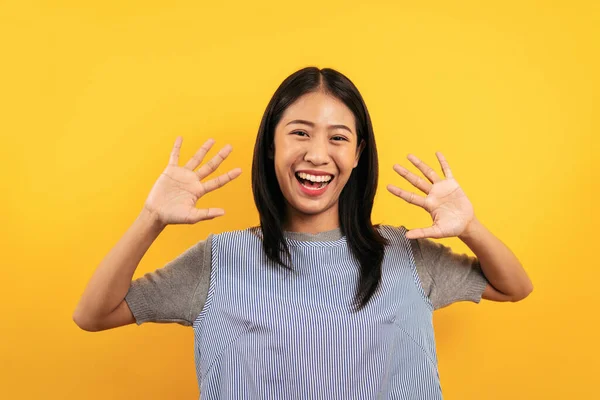 口を開けて笑顔で楽しみながら手を上げ黄色の背景に幸せを孤立させながら手を上げるカジュアルな服装の若いアジア人女性 — ストック写真