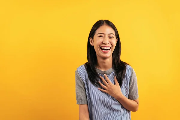若いですアジアの女性でカジュアル服に手を置きます胸と笑いラウドネス面白いですとともに冗談話を聞きながら黄色の背景に隔離 — ストック写真