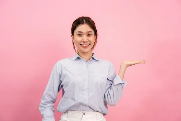 若いですアジアの女性身に着けています長い袖シャツと笑顔しながら一方を開いて提示し 広告ピンクの背景に隔離された何か — ストック写真