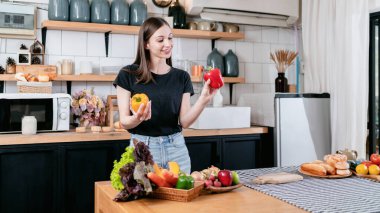 Elinde dolmalık biber tutan bir kadın taze sebze ve organik ürünlerle evde modern mutfakta sağlıklı yemek pişirmek için sofrada meyve hazırlarken keyif çatıyor..