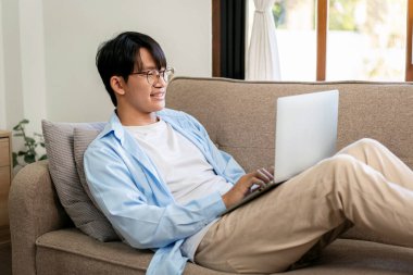 İş adamı rahat bir kanepede uzanıyor. İş arkadaşlarıyla görüşüp sohbet ederken evdeki video konferansında bilgisayarını kullanıyor..