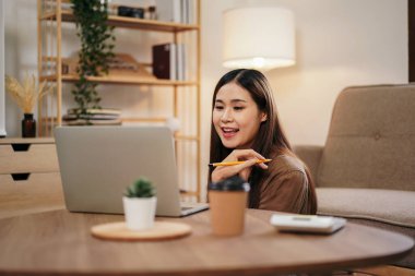 Çalışma ve video konferansı sırasında iş arkadaşlarıyla birlikte çalışan bayan girişimci ev ofisinin oturma odasında rahat bir şekilde oturmak üzere dizüstü bilgisayarla yeni iş projesini tartışıyor..