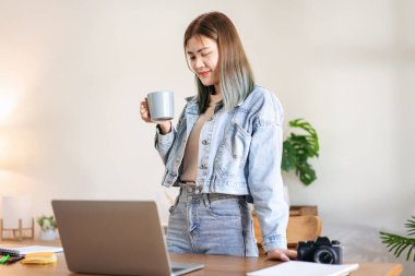 Kadın moda sanatçısı rahatlaması ve laptopta çalışırken kahve içmeye ara vermek ve atölyede yeni moda tasarımları yapmak..