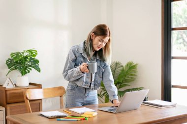 Kadın moda sanatçısı rahatlaması ve laptopta çalışırken kahve içmeye ara vermek ve atölyede yeni moda tasarımları yapmak..