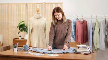 Kadın tasarımcı, ev atölyesinde yeni bir koleksiyon tasarlarken gömlek boyutunu ölçmek ve ayrıntıları kontrol etmek için mezura kullanıyor.