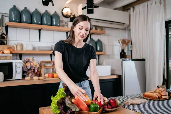 妇女拿着胡椒 一边享受着 一边准备新鲜蔬菜和水果 桌上放着有机食品 一边在家里现代厨房做饭 准备健康的饭菜 — 图库照片