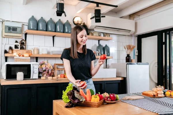 妇女手里拿着西红柿 一边享受着 一边准备蔬菜和水果 桌上放着有机食品 一边在家里的现代化厨房里做饭 准备健康的饭菜 — 图库照片