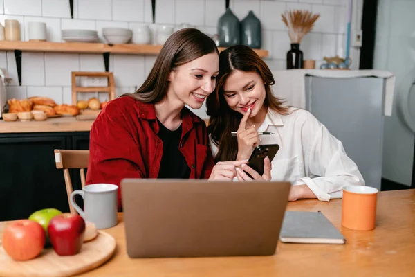 两名年轻女性使用智能手机搜索商业信息 一起阅读数据 在家里和桌上的笔记本电脑一起工作时 集思广益 讨论新的项目 — 图库照片