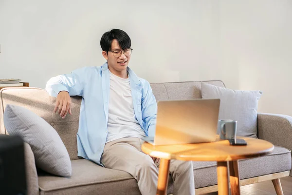 Businessman in casual is sitting to resting on comfortable sofa and watching entertainment on laptop while leisure with cozy lifestyle at home.