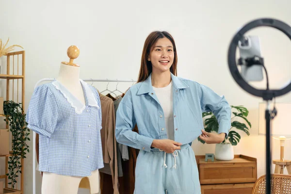 Female online seller is using smartphone to broadcast live on Vlog for introduce new fashions while presenting shirt collection and selling online clothing on social media.