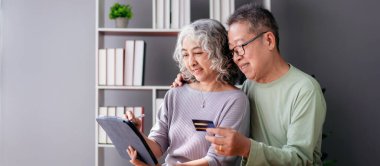 Üst düzey çift dijital tablet ve kredi kartını hayat sigortası almak ve internetten alışveriş yapmak için kullanırken aynı zamanda birlikte oturma odasında emeklilik aktivitesi yapmak için zaman geçiriyorlar..