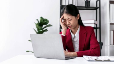 Takım elbiseli iş kadını stresli ve baş ağrısı içinde, modern çalışma ortamında çalışma masasında çalışırken yeni işlerin hesaplanması ve klavyede klavye ile bilgi yazma konusunda düşünceli..