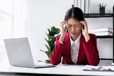 Takım elbiseli iş kadını stresli ve baş ağrısı içinde, modern çalışma ortamında çalışma masasında çalışırken yeni işlerin hesaplanması ve klavyede klavye ile bilgi yazma konusunda düşünceli..