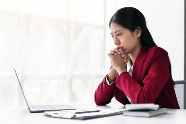 Takım elbiseli iş kadını, modern çalışma ortamında masa üzerinde çalışırken yeni iş dünyasının hesaplanması ve klavye ile bilgi yazma konusunda düşünceli ve stresli hissediyor.