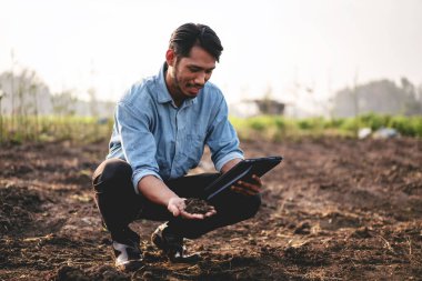 Smart farmer holding soil in his hand and using digital tablet to examining quality of soil for working and planning system control before vegetable growing with technology at agricultural field. clipart