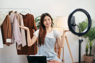 Kadın çevrimiçi satıcı, müşteriyle konuşmaya ve sosyal medyada çevrimiçi kıyafet satışına yeni koleksiyon sunarken canlı yayın yapmak için akıllı telefonu kullanıyor..
