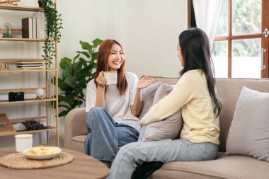 Genç lezbiyen çift kahve içip rahatlamak için evdeki büyük rahat kanepede sohbet ediyor ve birlikte gülüyorlar..