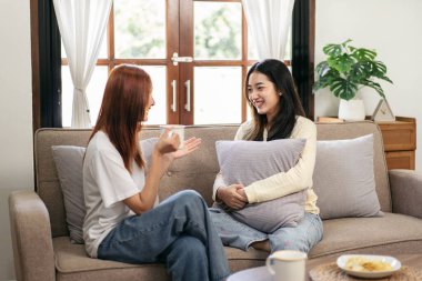 Genç lezbiyen çift kahve içip rahatlamak için evdeki büyük rahat kanepede sohbet ediyor ve birlikte gülüyorlar..