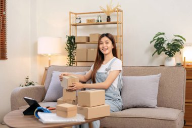 Genç girişimci ürünleri karton kutulara dolduruyor. Müşteriye ev teslimi hazırlamak için. Koltukta rahat bir şekilde otururken ve ev ofisinin oturma odasında çalışırken..