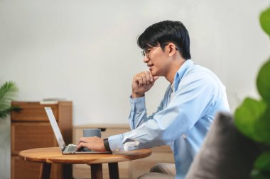 Gündelik iş adamı rahat bir koltukta oturup yeni iş için düşünceli bir fikirle evde iş projesi hakkında bilgi yazmak ve çalışmak için dizüstü bilgisayar kullanıyor..