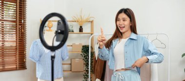 Kadın çevrimiçi satıcı, tişört koleksiyonu yapmak ve sosyal medyada çevrimiçi kıyafet satmak için başparmak kaldırırken canlı yayın yapmak için akıllı telefon kullanıyor.