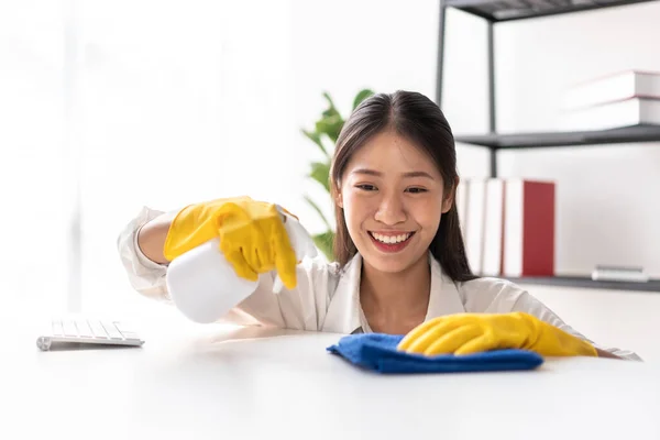 テーブルの上に衛生スプレーを噴霧するために手袋を着用エプロンの主婦と家の中で働くと掃除しながら 家具をきれいにするためにマイクロファイバーファブリックを使用して — ストック写真