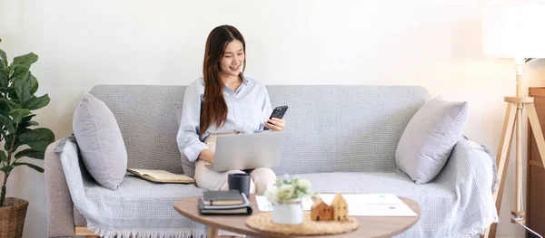 Női Szabadúszó Üzleti Adatokat Olvas Okostelefonon Gépel Laptopon Miközben Kényelmesen — Stock Fotó
