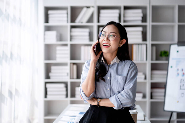 Accounting business concept, Accountant woman smiling and using smartphone to talking with partners about finance data while working to analyzing about investment with business planning finance.