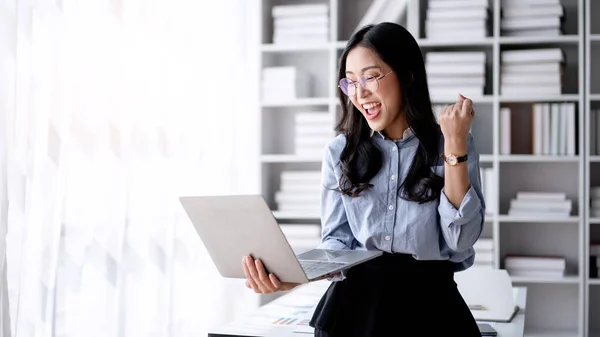 会计行业的概念 会计女性在用笔记本电脑读到好消息时 一边兴奋地举起拳头庆祝自己的成就 一边用商业计划书输入投资信息 — 图库照片